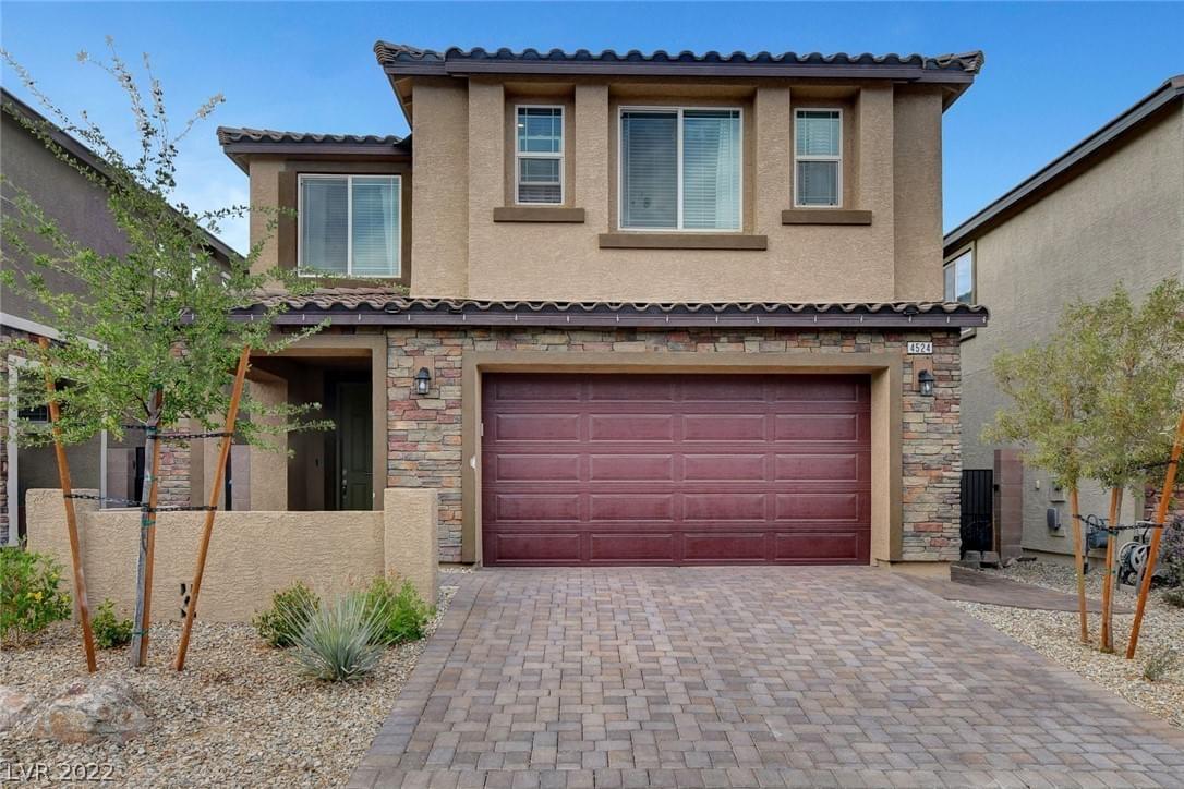 A light brown stucco home with flat top roof, red garage door, baby desert trees, stone facade, stone front drive